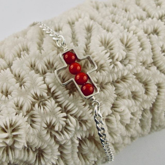 Une chaîne maille gourmette et 4 perles 4 mm de véritable corail rouge de Méditerranée, délicatement enchâssées dans une croix ajourée,  en argent 925/1000e